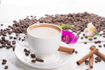 white cup of coffee on a background of scattered coffee beans on a white background
