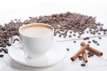 white cup of coffee on a background of scattered coffee beans on a white background