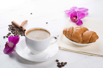 cup of coffee and a croissant on a served table with flower buds
