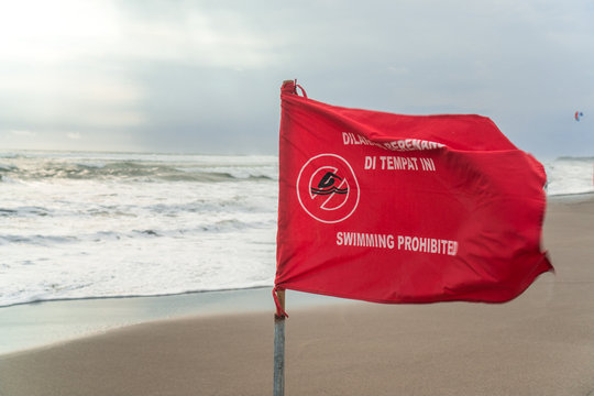 Red flag with swimming warning waving in the wind on the beach