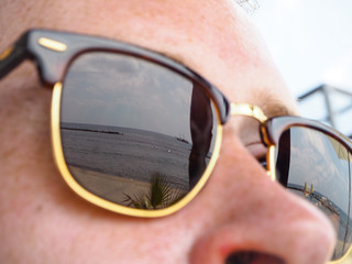 Mediterranean coast with passing ship reflected in male sunglasses