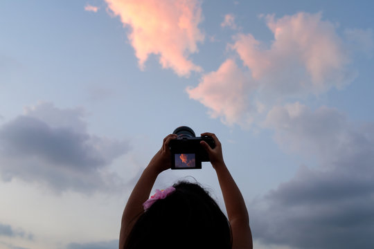 Little girl taking picture of the clouds at sunset