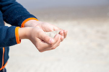 a little boy slowly lets sand flow through his hands scattered by the wind.