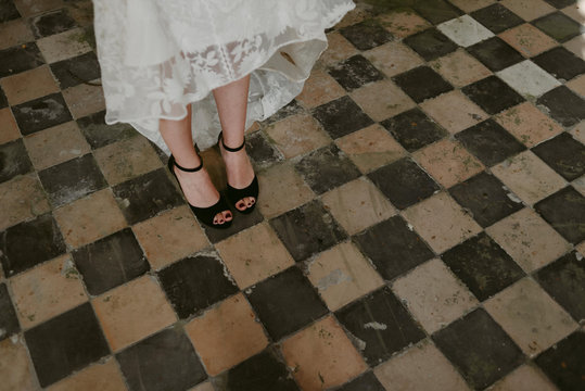 Bride in black peep toe wedding shoes and lace dress on old checkered tile