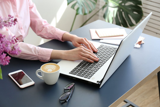 Feminine freelance workspace concept. Woman's hands typing on white laptopp with black keyboard, desk with matte blue table top. Freelance blogger writing an article. Close up, copy space for text.