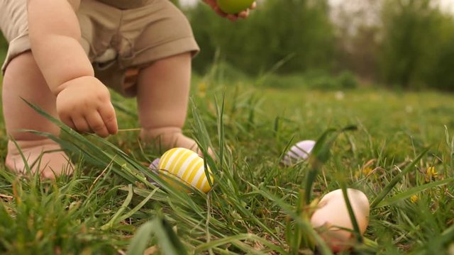 Close-up of baby legs. A child is looking for Easter eggs in the grass. Happy easter family
