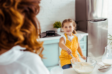selective focus of smiling kid in apron preparing dough in kitchen
