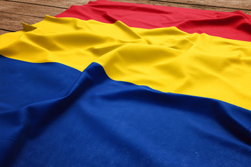 Flag of Romania on a wooden desk background. Silk Romanian flag top view.