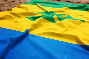 Flag of Saint Vincent And The Grenadines on a wooden desk background. Silk flag top view.