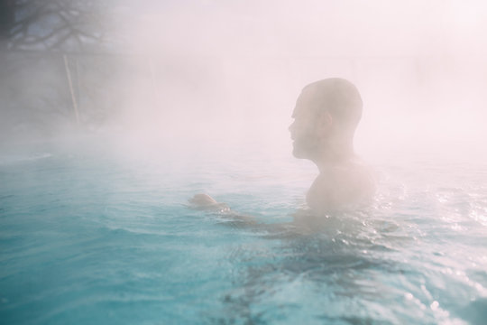 Young man swimming in a pool during cold winter days