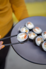 A stylish young smiling girl poses for a photo and holding in her hand a plate of rolls and chopsticks in the other hand. Appetizing advertising photography for restaurant, sushi bar, delivery