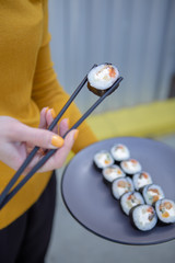 A stylish young smiling girl poses for a photo and holding in her hand a plate of rolls and chopsticks in the other hand. Appetizing advertising photography for restaurant, sushi bar, delivery