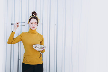 A stylish young smiling girl poses for a photo and holding in her hand a plate of rolls and chopsticks in the other hand. Appetizing advertising photography for restaurant, sushi bar, delivery
