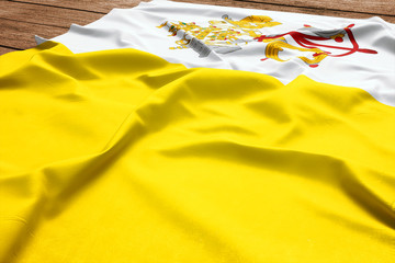 Flag of Vatican City (Holy See) on a wooden desk background. Silk flag top view.