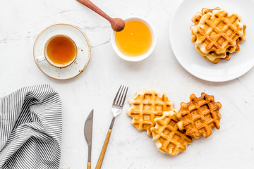 Breakfast with Belgian waffles with honey, tea, knife, fork and spoon on white marble background top view