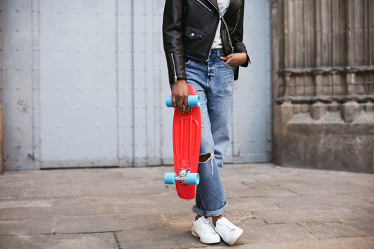 Cool woman holding a red skateboard in the city.