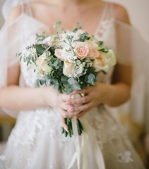 Bride in a wedding dress holding a wedding bouquet in her hands close-up