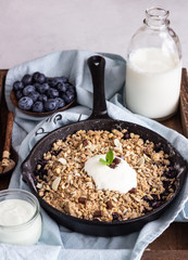 Oatmeal crumble in cast iron pan with fresh blueberry and natural yogurt. Healthy food concept. 