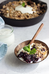 Oatmeal crumble in cast iron pan with fresh blueberry and natural yogurt. Healthy food concept. 