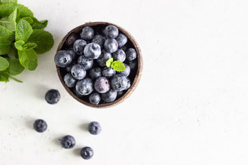 Wooden bowl of fresh blueberries on light grey stone table. Healthy organic seasonal fruit background. 
