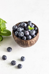 Wooden bowl of fresh blueberries on light grey stone table. Healthy organic seasonal fruit background. 