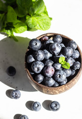 Wooden bowl of fresh blueberries on light grey stone table. Healthy organic seasonal fruit background. 