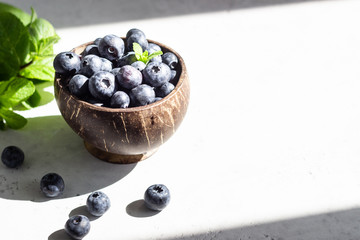 Wooden bowl of fresh blueberries on light grey stone table. Healthy organic seasonal fruit background. 