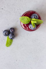 Delicious blueberry smoothie with fresh berries and mint in glass jars. Summer healthy drink. Grey stone background. Copy space.
