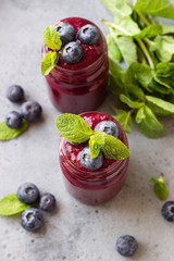 Delicious blueberry smoothie with fresh berries and mint in glass jars. Summer healthy drink. Grey stone background. Copy space.