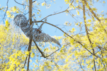 A doll from proaloki rides on a swing, against the sky and branches with green foliage.
