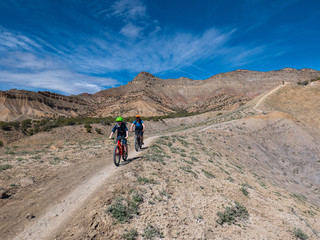 Obraz premium A little boy mountain bikes on singletrack trail with his mother