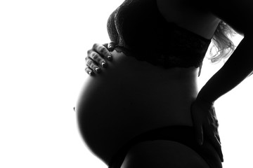 Black and white image of woman tenderly holding her pregnant belly attentively turning to her unborn child. Concept of pregnancy and happy motherhood.