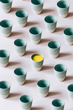 Pattern of empty mugs with just one mug with golden milk