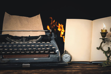 Typewriter and blank open book page on a writer desk on a burning fire background.