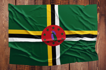 Flag of Dominica on a wooden table background. Wrinkled Dominican flag top view.