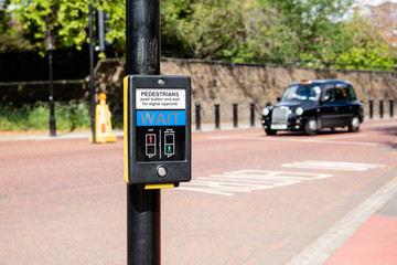 Traffic light for pedastrians in UK (Britain) for safe road crossing; blured taxi in the background
