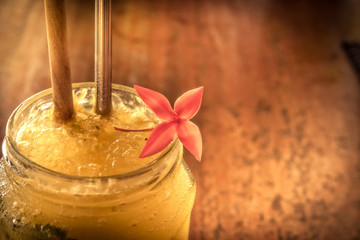 Tropical cocktail in glass jar with flower and straw in vintage vibrant orange yellow colors on wooden bar counter retro style