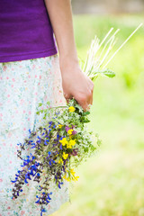 The girl is holding out a bouquet of wildflowers.