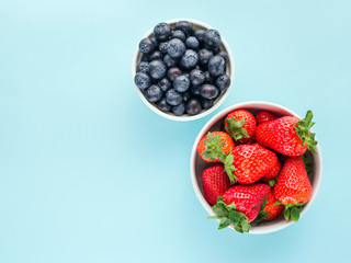 Strawberries and blueberries in white bowls on a blue bright background, top view