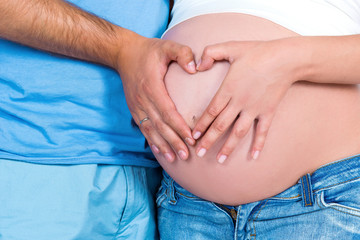 Parental love and happy motherhood. Closeup of heart shape on the background of a pregnant tummy.