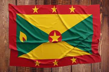 Flag of Grenada on a wooden table background. Wrinkled Grenadan flag top view.