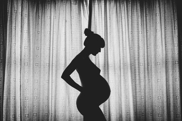 Silhouette of a nude pregnant woman in the window of her home