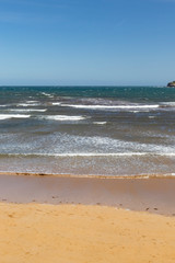 Stunning view of the ocean calm surf with quiet waves reaching the sandy shore and clear turquoise water and clear skies.
