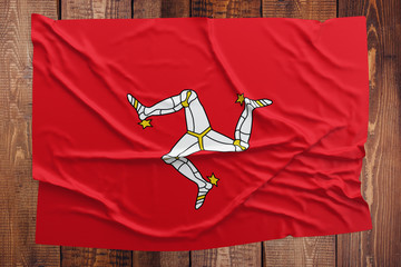 Flag of Isle Of Man on a wooden table background. Wrinkled flag top view.