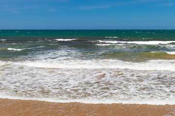 Stunning view of the ocean calm surf with quiet waves reaching the sandy shore and clear turquoise water and clear skies.