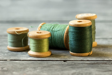 Fototapeta na wymiar Sewing kit. Spools of green thread on old wooden table.