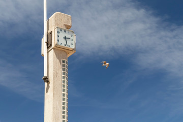 Fototapeta na wymiar Concrete stella on the beach with a clock and a flag on the ocean