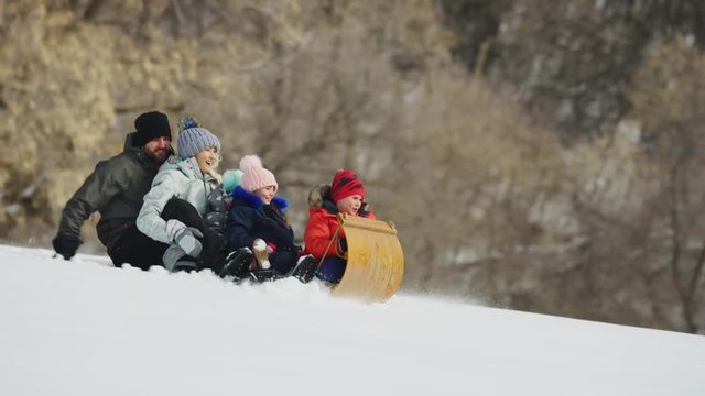 Slow motion tracking shot of family riding toboggan downhill in winter snow / South Fork, Utah, United States