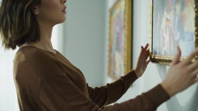 Close up of woman hanging paintings on wall then smiling / Cedar Hills, Utah, United States
