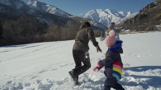Slow motion of mother and daughter having snowball fight with man near mountain / South Fork, Utah, United States